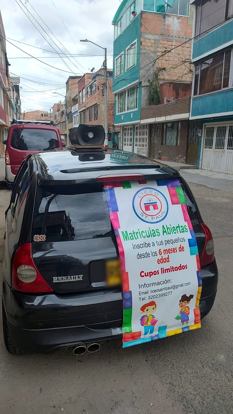 Carro de perifoneo con parlantes y pendón de matrículas abiertas de un colegio