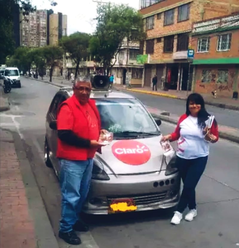 Equipo con volantes junto al carro de perifoneo con la marca de un cliente en el capó