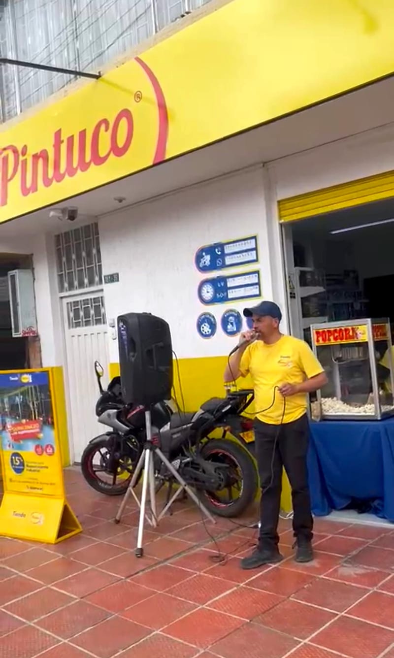 Locutor de Publimao con micrófono y parlante en trípode haciendo perifoneo frente a una tienda